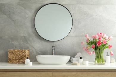 Vase with beautiful pink tulips and toiletries near sink in bathroom