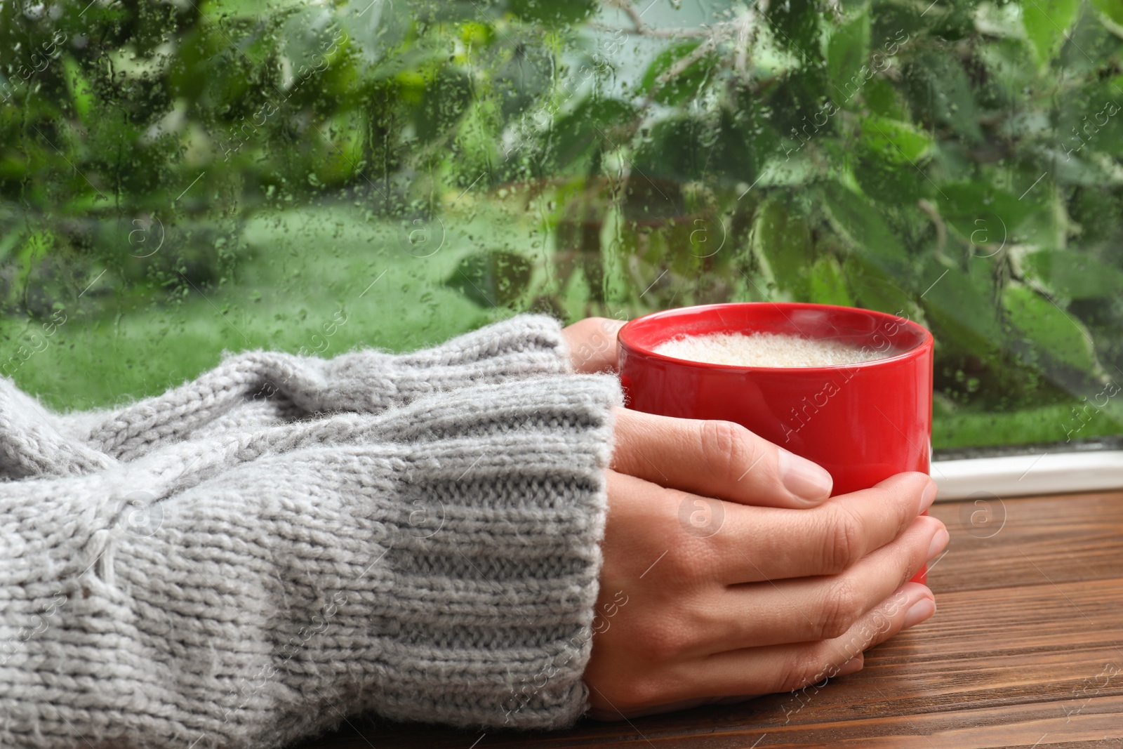 Photo of Woman with cup of coffee near window on rainy day, closeup