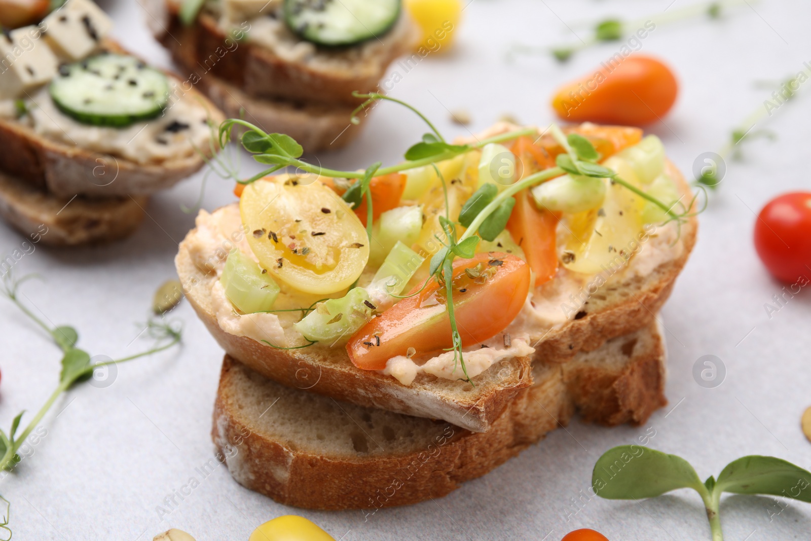 Photo of Tasty vegan sandwiches with vegetables on light grey table, closeup