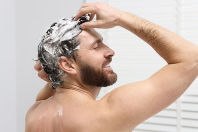 Photo of Happy man washing his hair with shampoo in shower