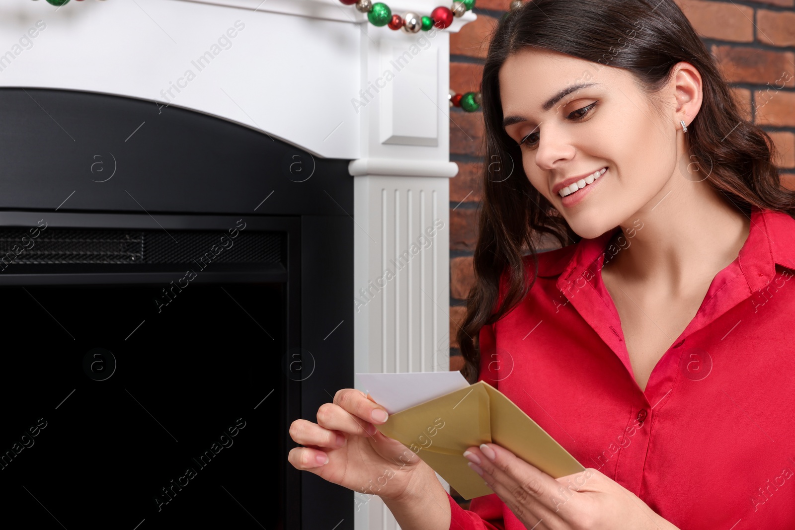 Photo of Young woman with greeting card sitting near fireplace indoors