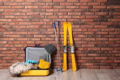 Photo of Suitcase with clothes, camera and skis on floor against brick wall, space for text. Winter vacation