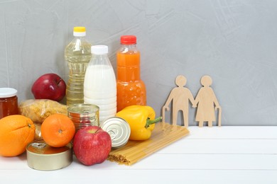 Photo of Humanitarian aid for elderly people. Different donation food products and figures of senior couple on white wooden table