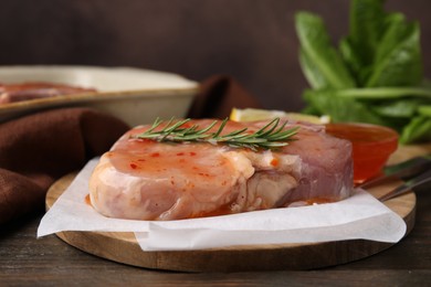 Board with raw marinated meat and rosemary on wooden table, closeup