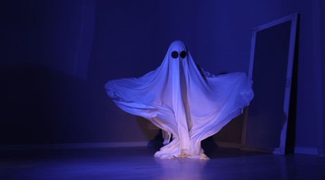 Photo of Creepy ghost. Woman covered with sheet in blue light, space for text