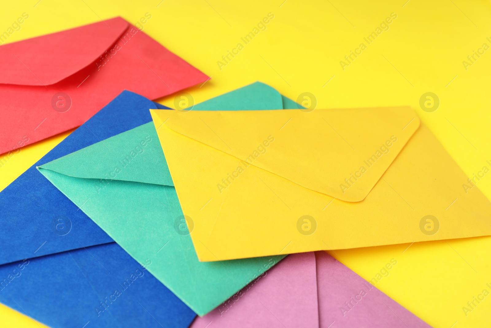 Photo of Colorful paper envelopes on yellow background, closeup