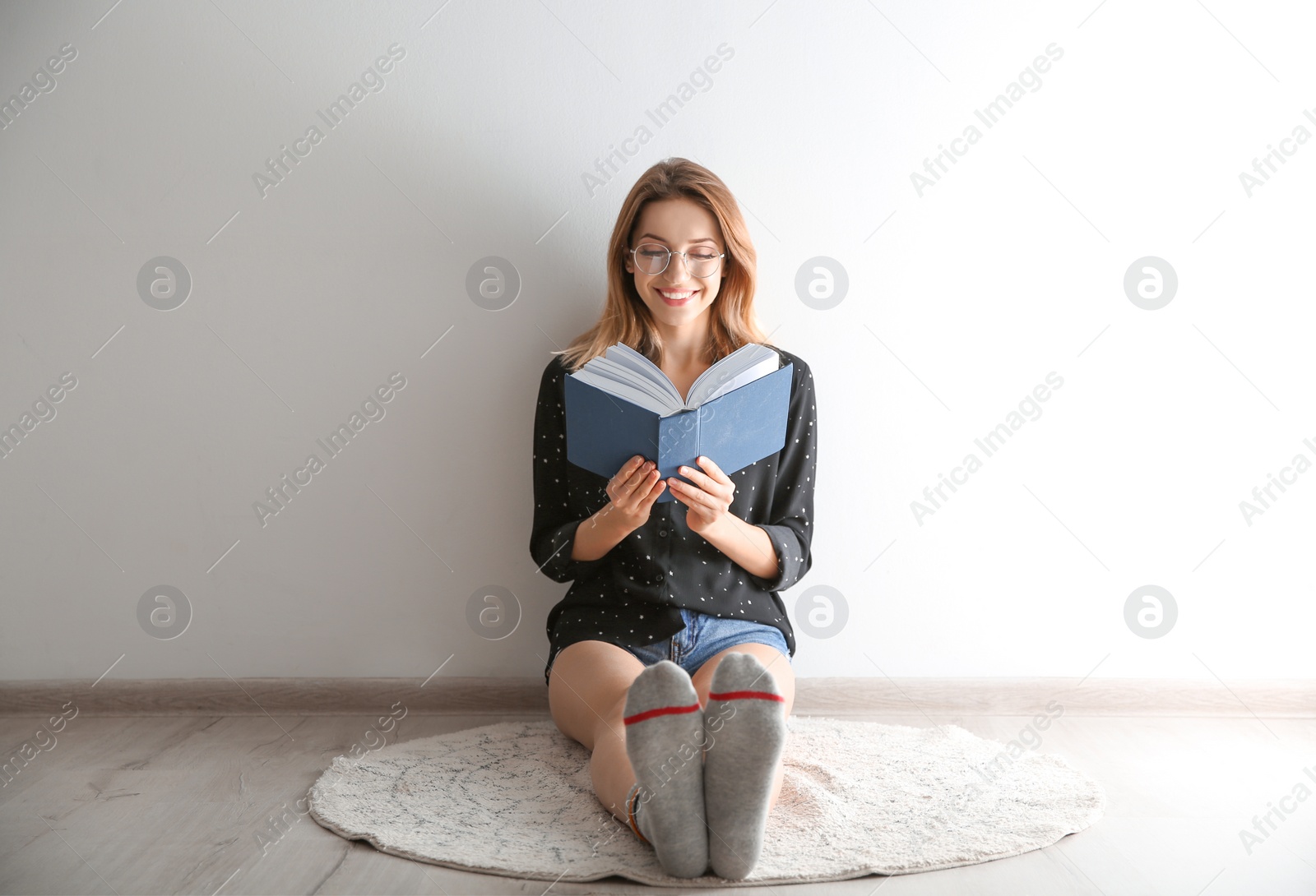 Photo of Young woman reading book on floor near wall