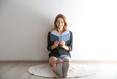 Young woman reading book on floor near wall