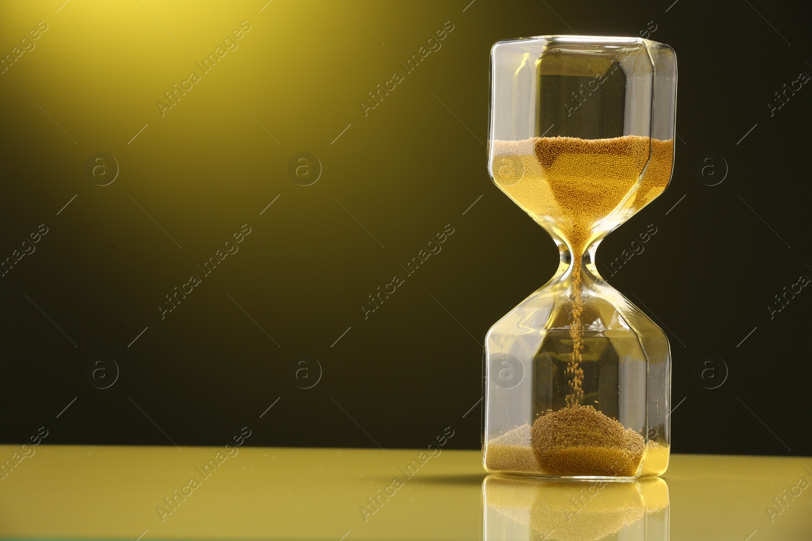 Photo of Hourglass with flowing sand on color background. Space for text