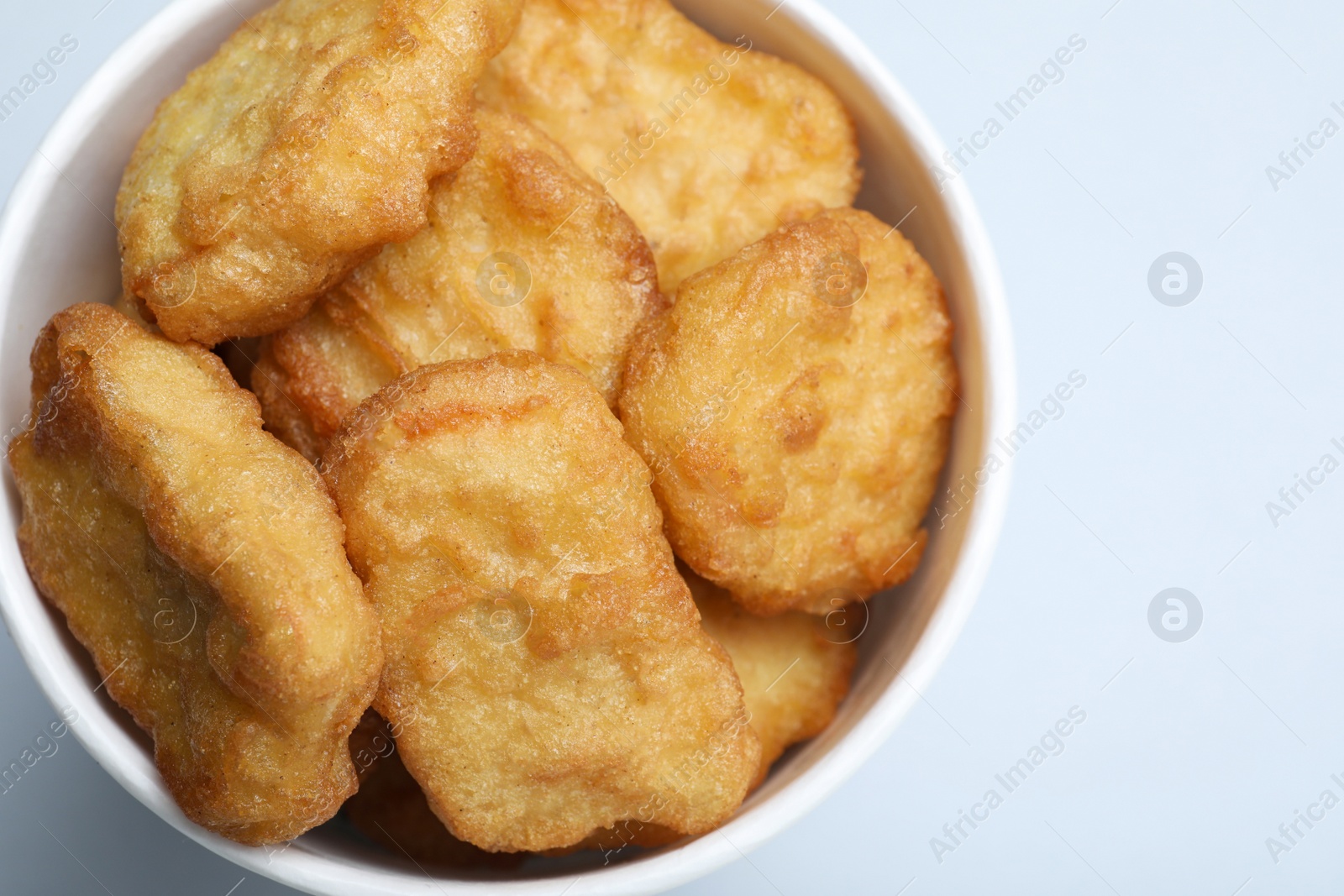 Photo of Bucket with delicious chicken nuggets on light background, closeup