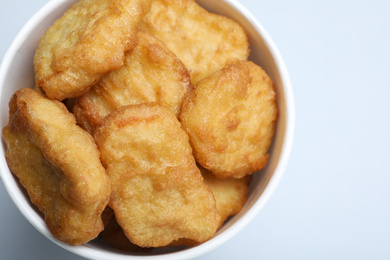 Photo of Bucket with delicious chicken nuggets on light background, closeup