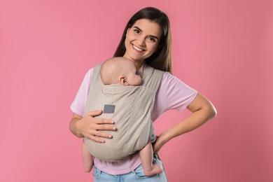 Photo of Mother holding her child in sling (baby carrier) on pink background