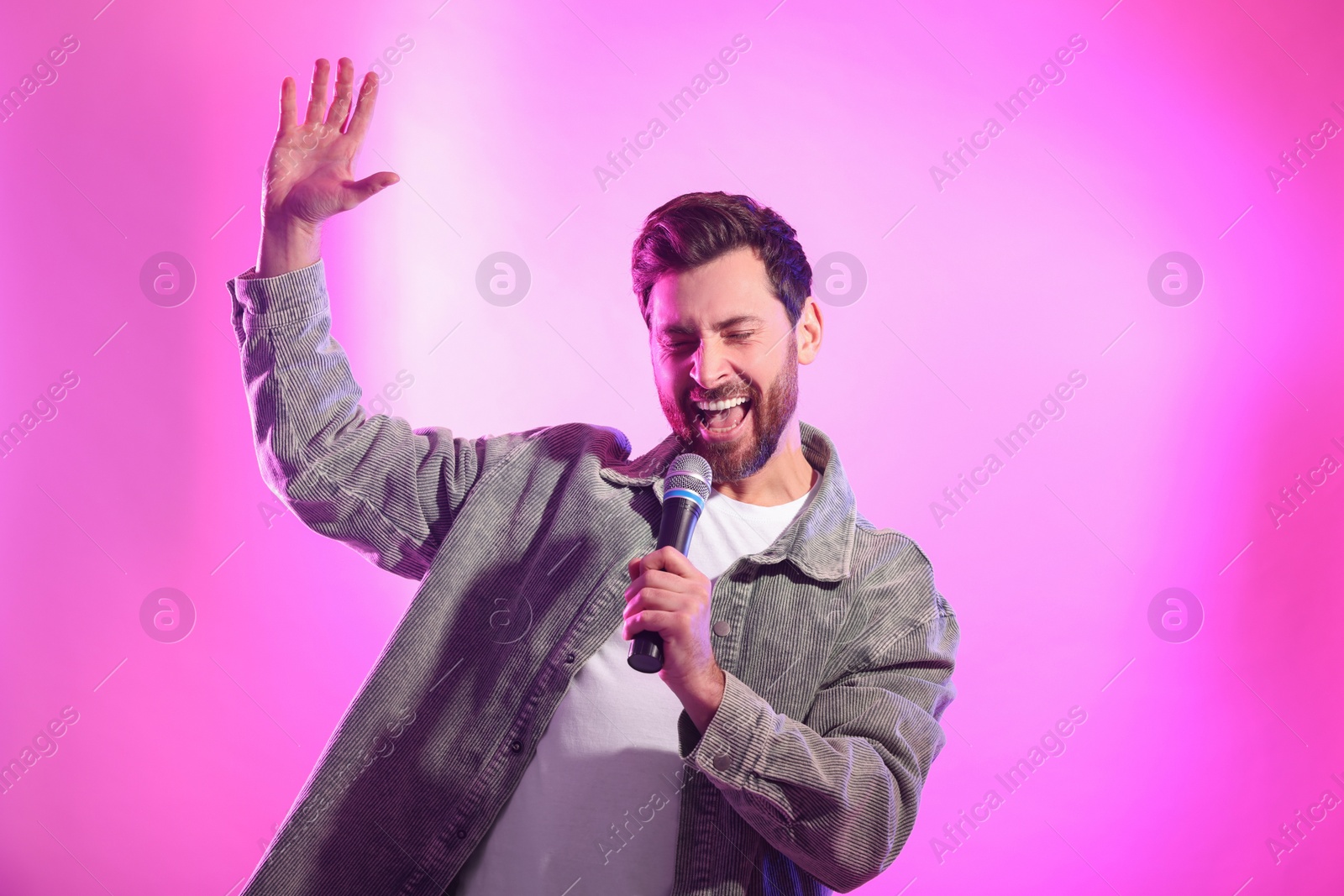 Photo of Handsome man with microphone singing on pink background