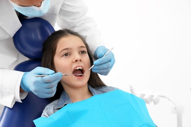 Photo of Professional dentist working with little girl in clinic. Space for text
