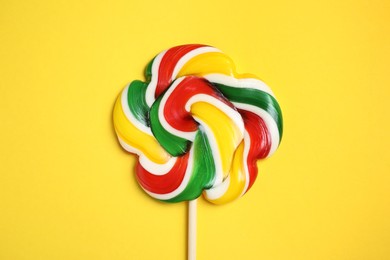 Stick with bright lollipop on yellow background, top view