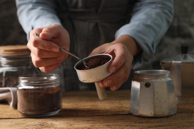 Photo of Woman putting ground coffee in moka pot at wooden table, closeup