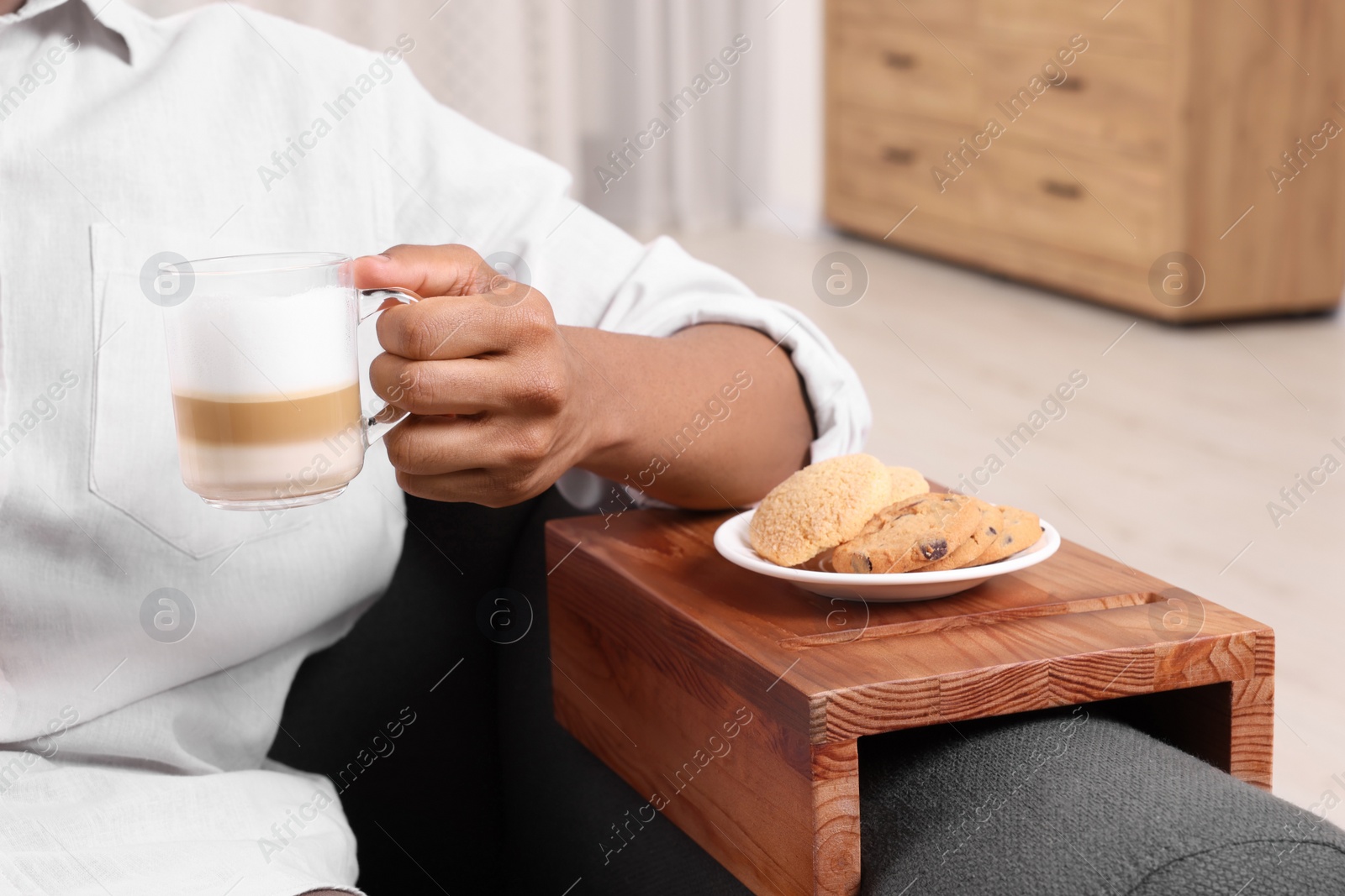 Photo of Cookies on sofa armrest wooden table. Man holding cup of coffee at home, closeup