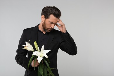 Photo of Sad man with white lilies mourning on light grey background, space for text. Funeral ceremony