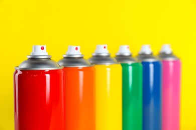 Colorful cans of spray paints on yellow background, closeup