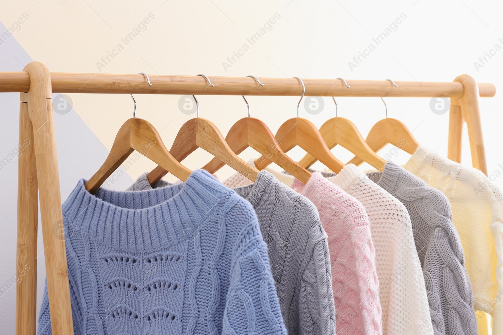 Photo of Collection of warm sweaters hanging on rack near color wall