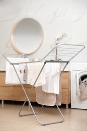 Photo of Clean laundry hanging on drying rack in bathroom