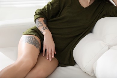 Photo of Beautiful woman with tattoos on body resting in living room, closeup