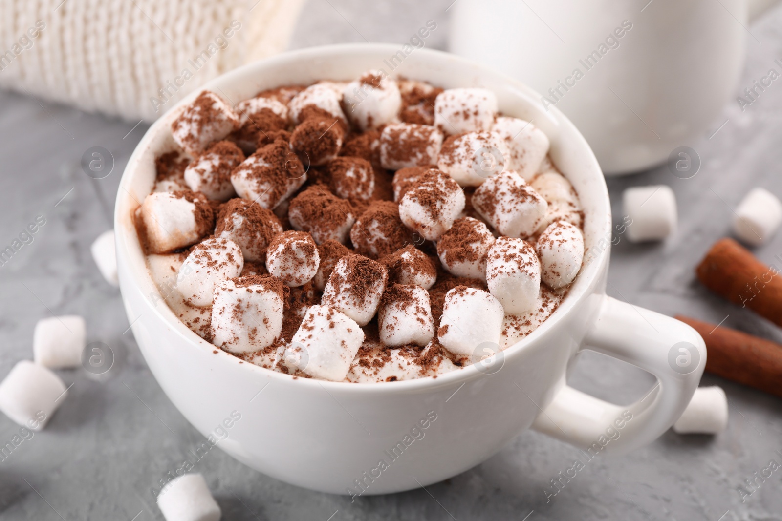 Photo of Cup of aromatic hot chocolate with marshmallows and cocoa powder on gray table, closeup