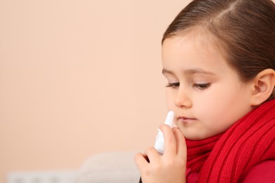 Photo of Cute little girl holding nasal spray on beige background, space for text