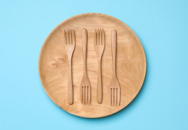 Photo of Wooden plate with forks on light blue background, top view. Cooking utensils