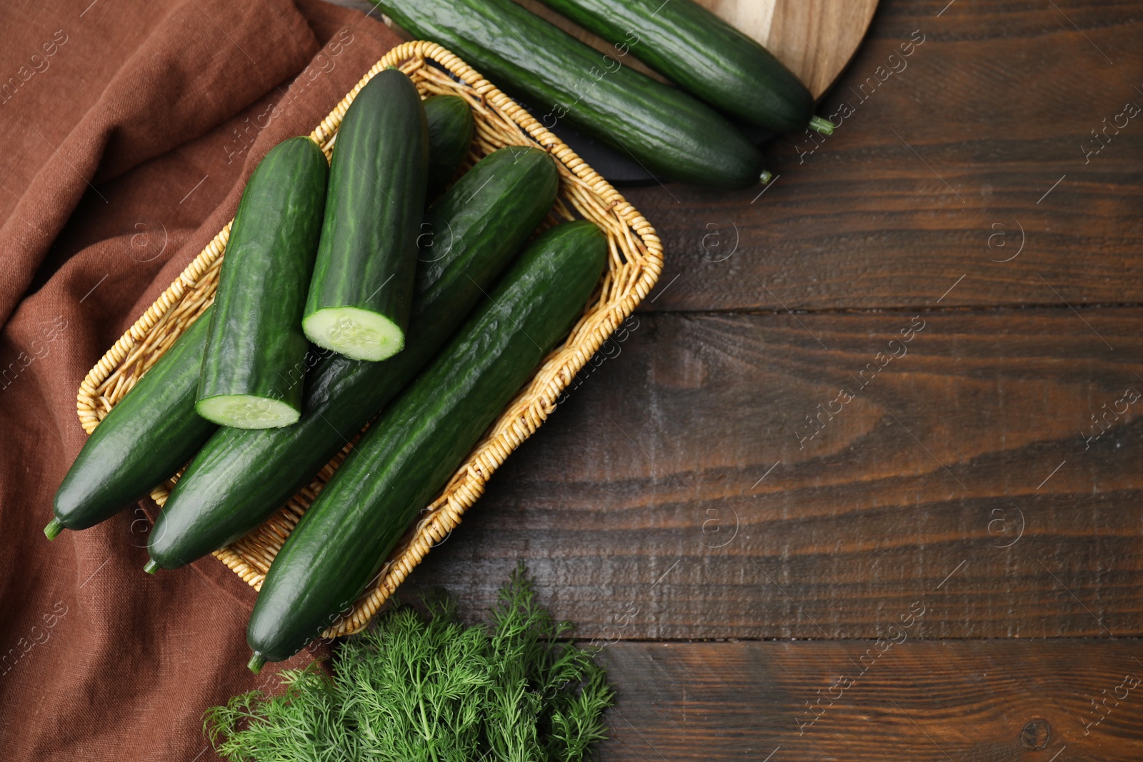 Photo of Fresh cucumbers in wicker basket and dill on wooden table, flat lay. Space for text