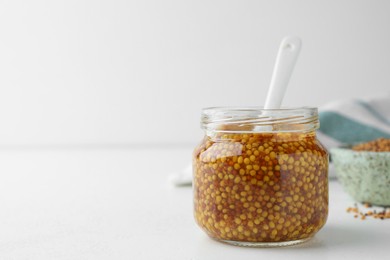 Photo of Whole grain mustard and spoon in jar on white table. Space for text