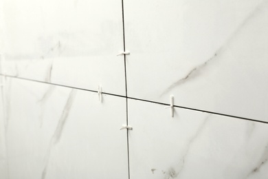 Photo of Closeup view of ceramic tiles with plastic crosses in joints on wall. Building and renovation works