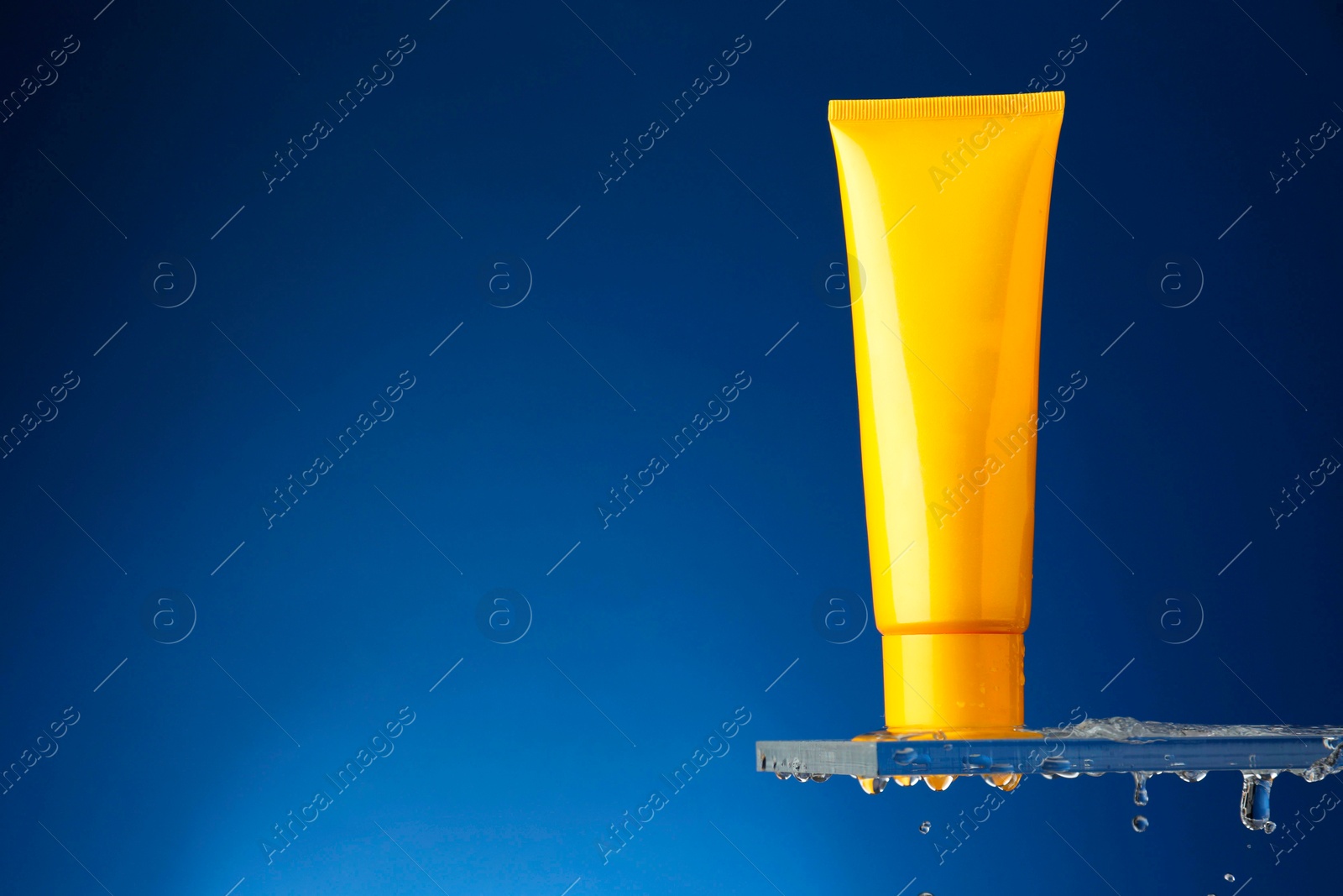 Photo of Moisturizing cream in tube on glass with water drops against blue background. Space for text