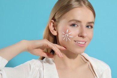 Beautiful young woman with sun protection cream on her face against light blue background