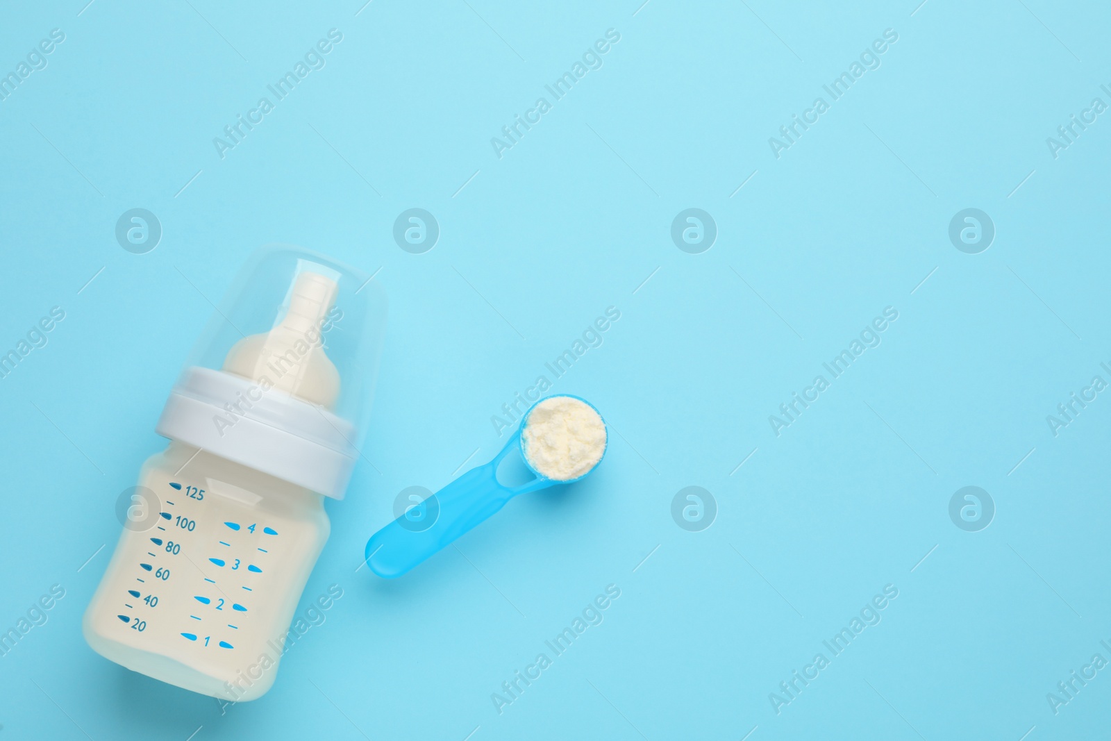 Photo of Feeding bottle with infant formula and powder on light blue background, flat lay. Space for text