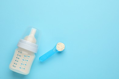 Feeding bottle with infant formula and powder on light blue background, flat lay. Space for text