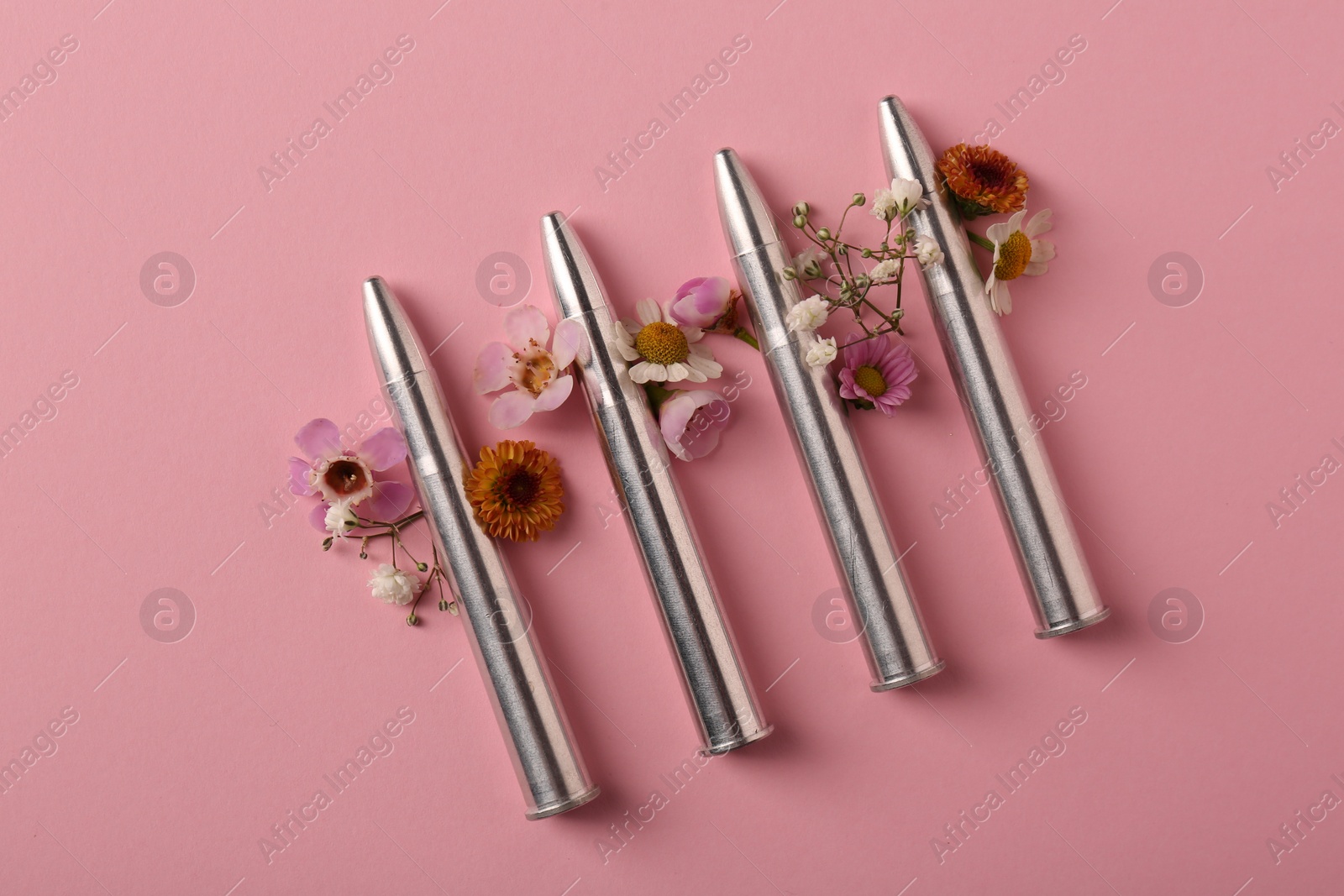 Photo of Metal bullets and beautiful flowers on pink background, flat lay