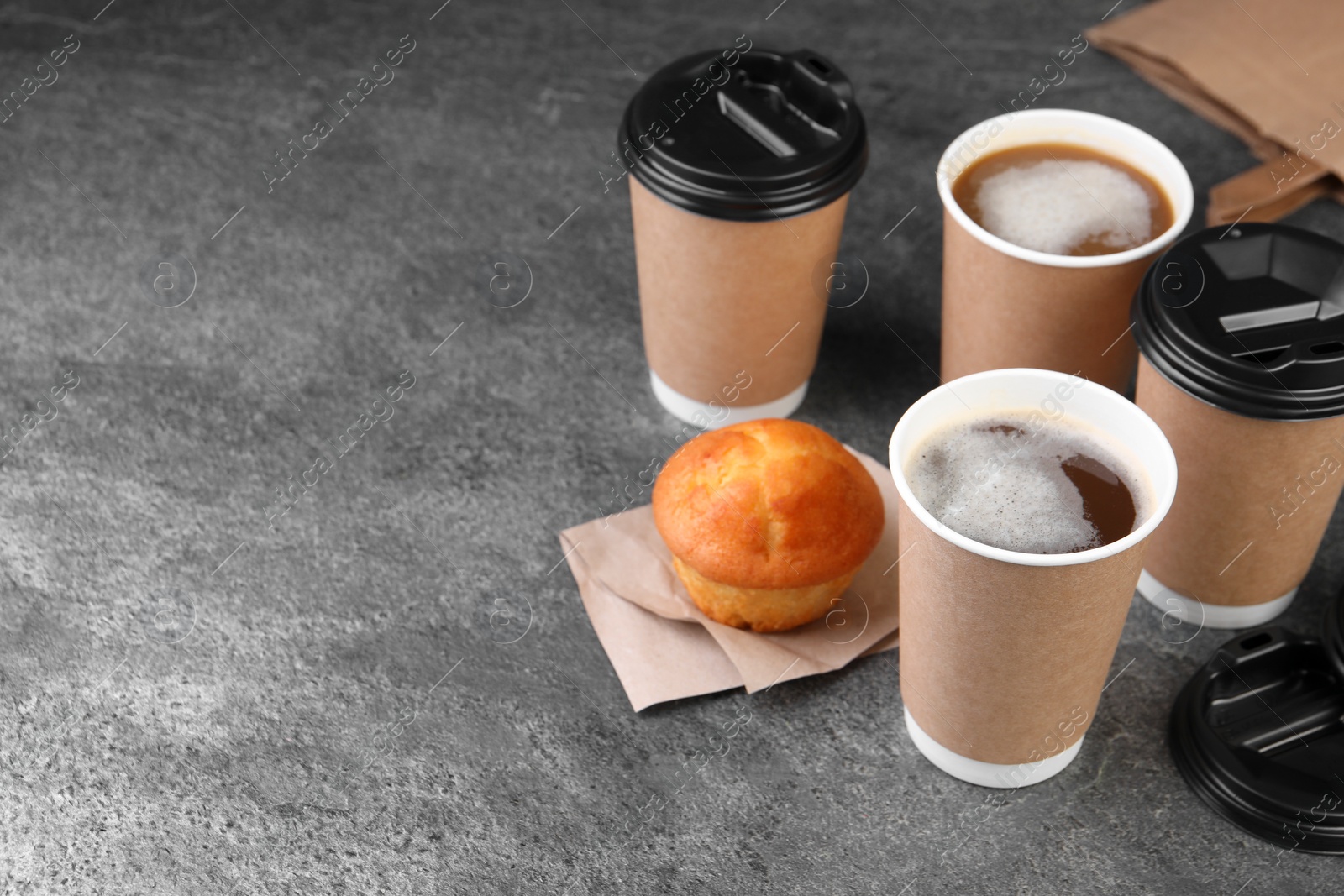 Photo of Coffee to go. Paper cups with tasty drink and muffin on grey textured table, space for text