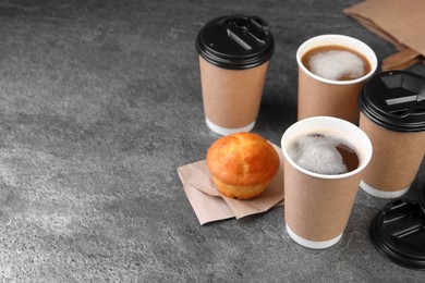 Photo of Coffee to go. Paper cups with tasty drink and muffin on grey textured table, space for text