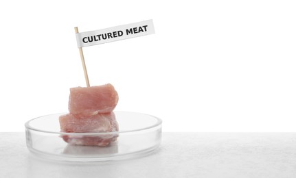 Pieces of raw cultured meat with toothpick label in Petri dish on table against white background, space for text