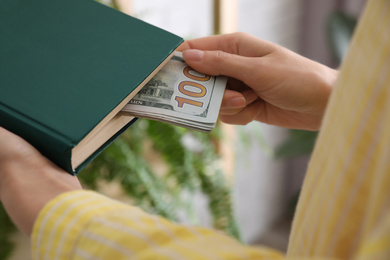 Photo of Woman hiding dollar banknotes in book indoors, closeup. Money savings