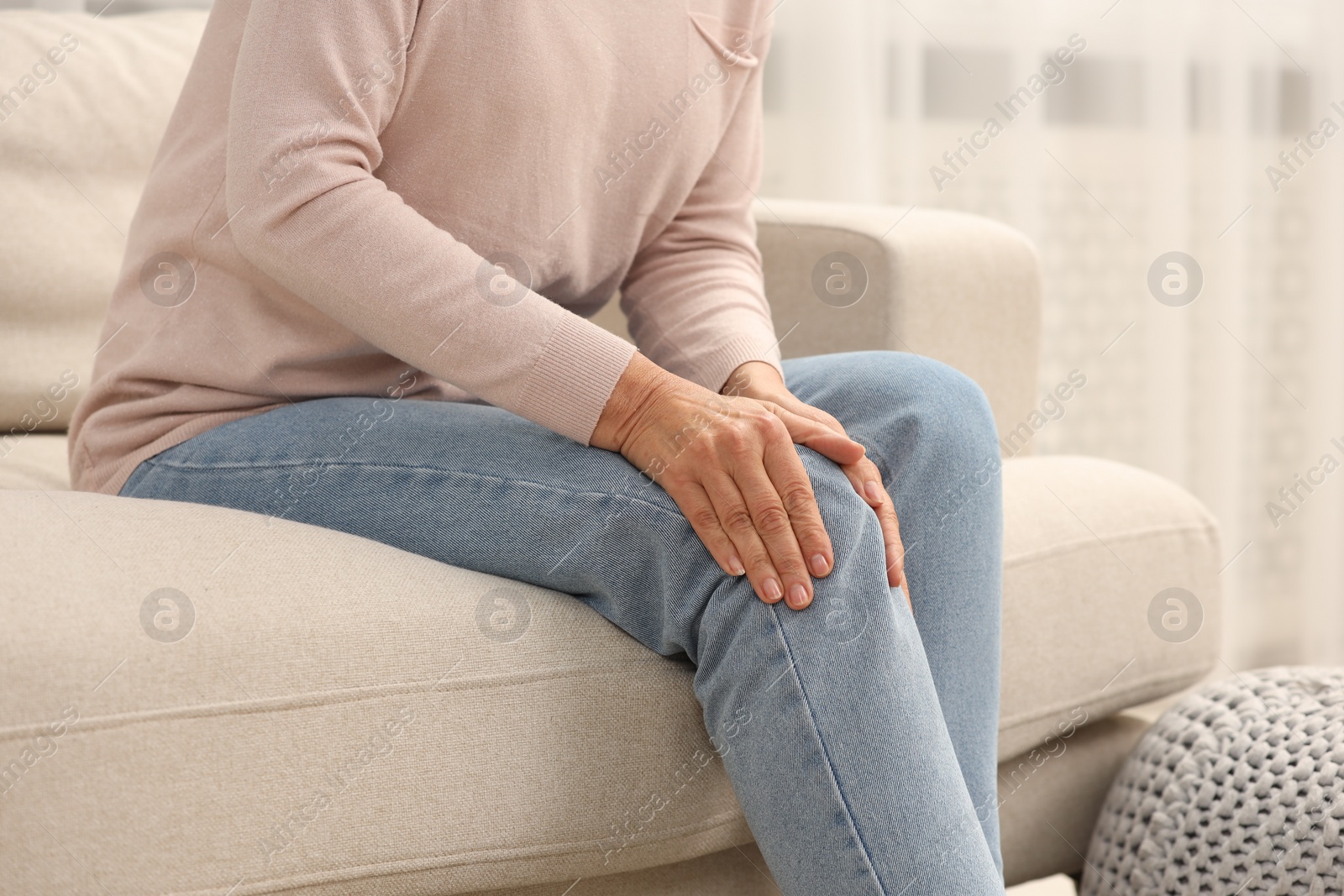 Photo of Mature woman suffering from knee pain on sofa at home, closeup. Rheumatism symptom