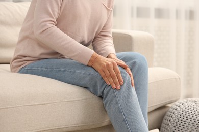 Photo of Mature woman suffering from knee pain on sofa at home, closeup. Rheumatism symptom