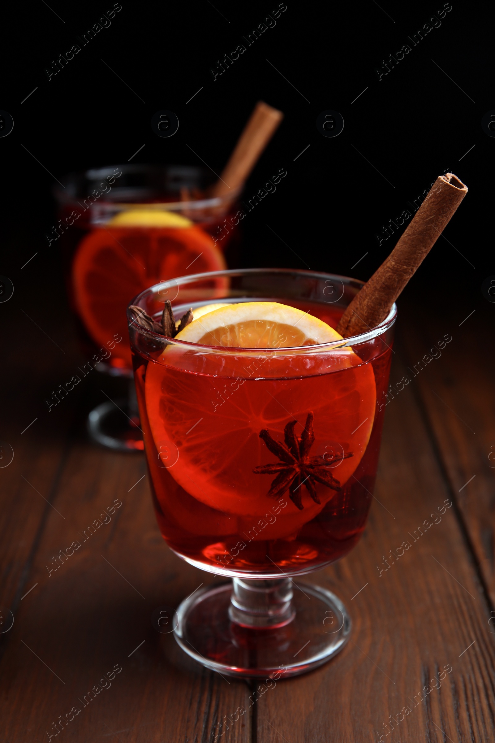 Photo of Glasses with red mulled wine on wooden table against dark background