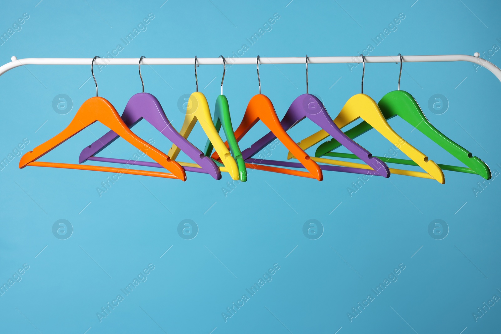 Photo of Bright clothes hangers on metal rail against light blue background