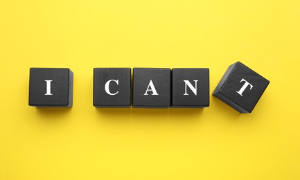 Photo of Motivation concept. Changing phrase from I Can't into I Can by removing black wooden cube with letter T on yellow background, flat lay