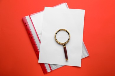 Photo of Magnifying glass, sheet of paper and folder on red background, top view