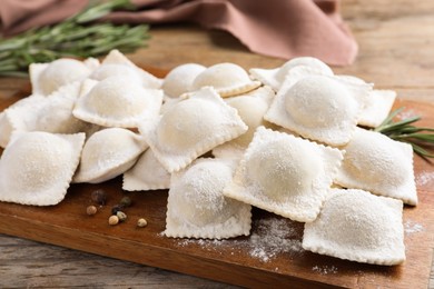 Photo of Uncooked ravioli and rosemary on wooden table, closeup