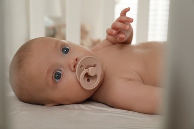 Photo of Cute little baby with pacifier lying in crib