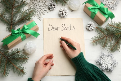 Photo of Top view of woman writing letter to Santa at white wooden table, closeup